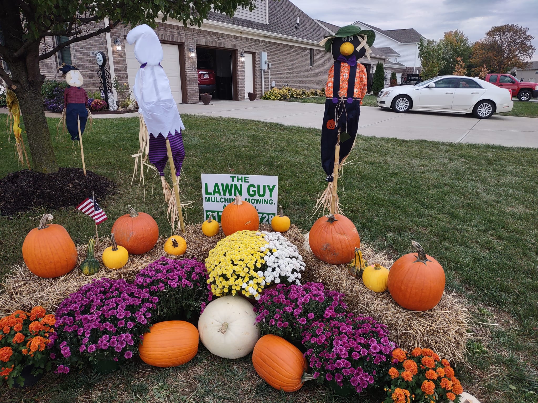 Fall landscaping display with pumpkins, mums, and scarecrows